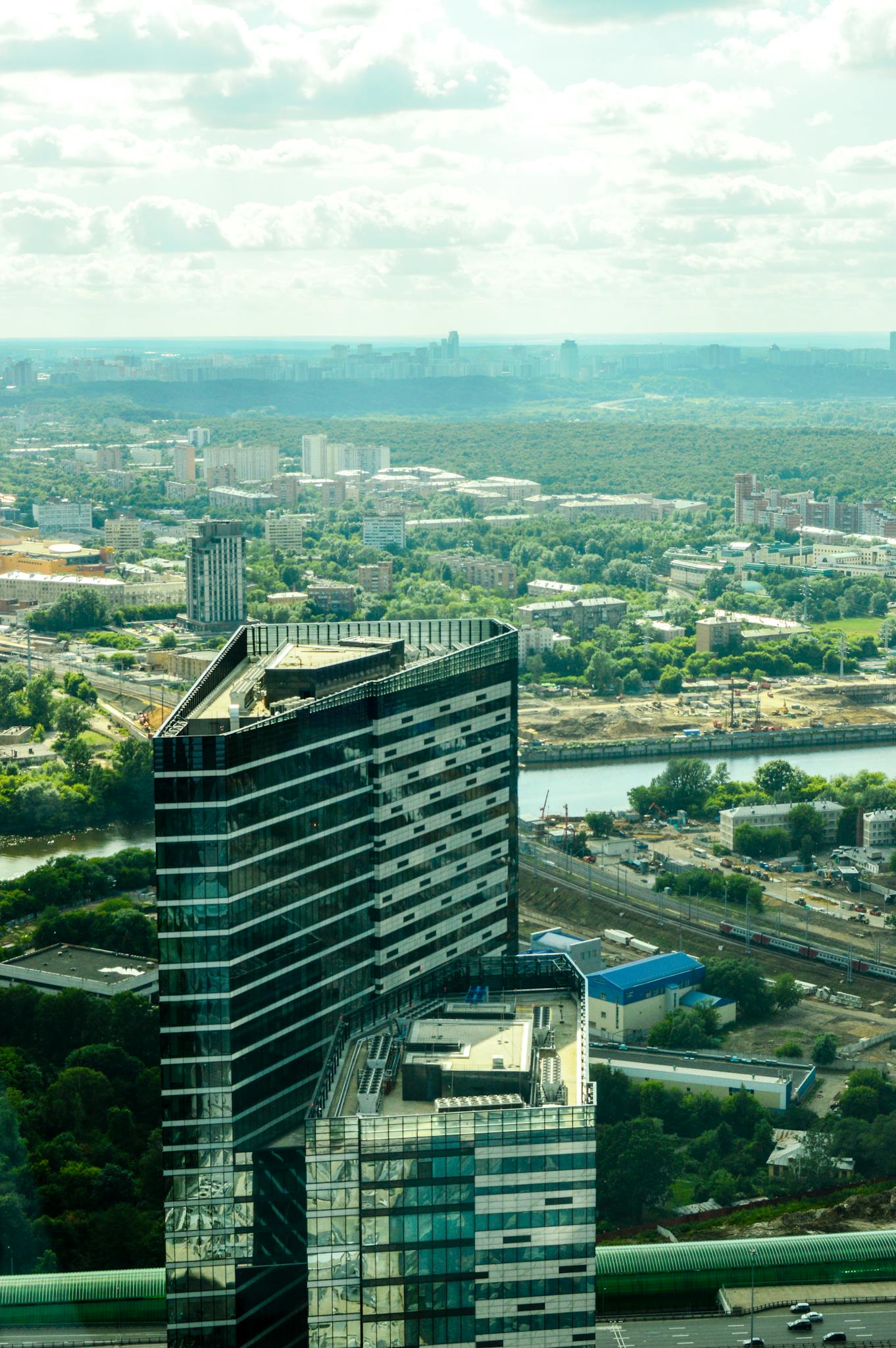 Aerial view of a modern skyscraper in a vibrant city with lush greenery and urban development.