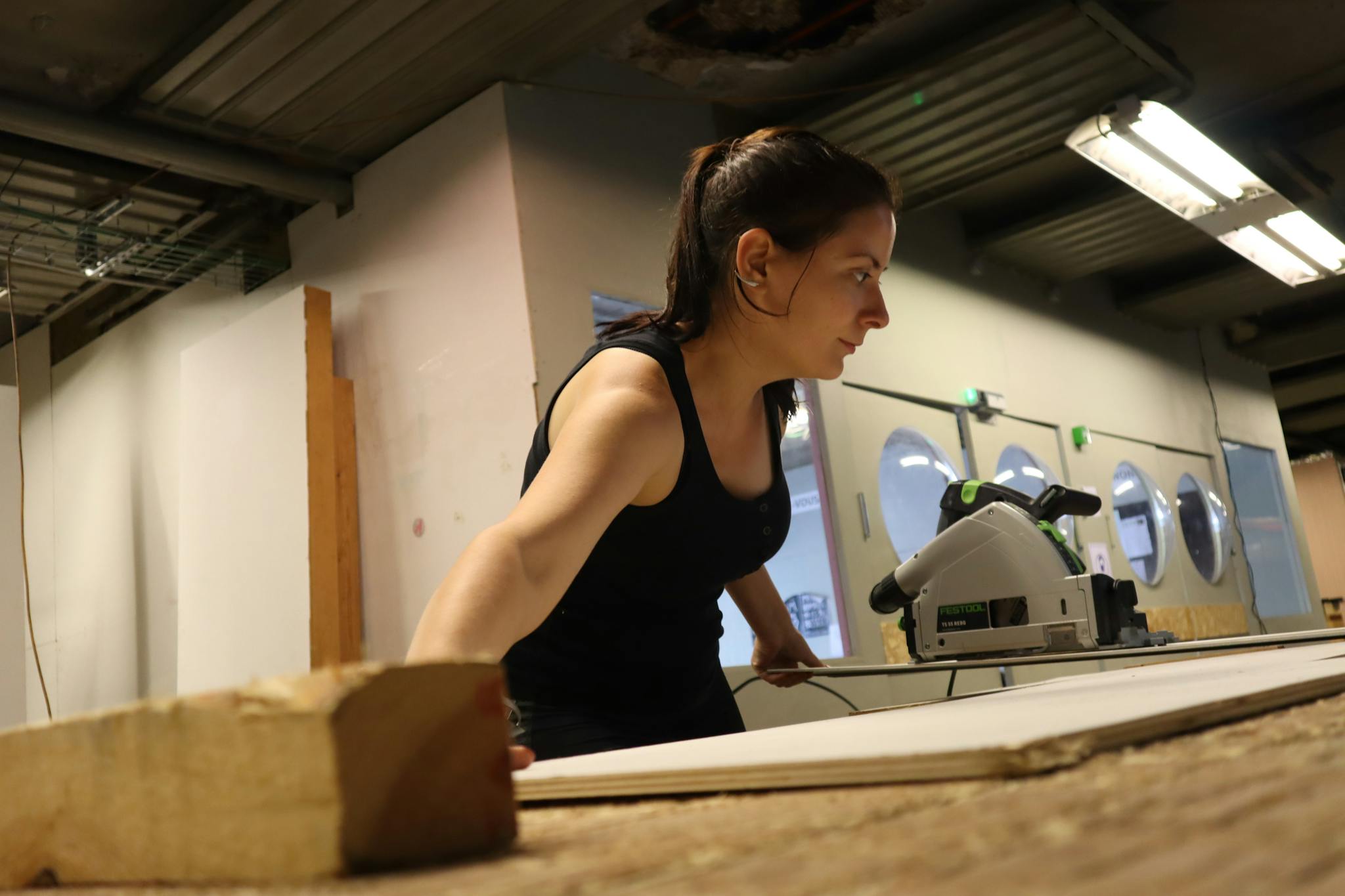 Woman woodworking indoors, using tools in a workshop setting.